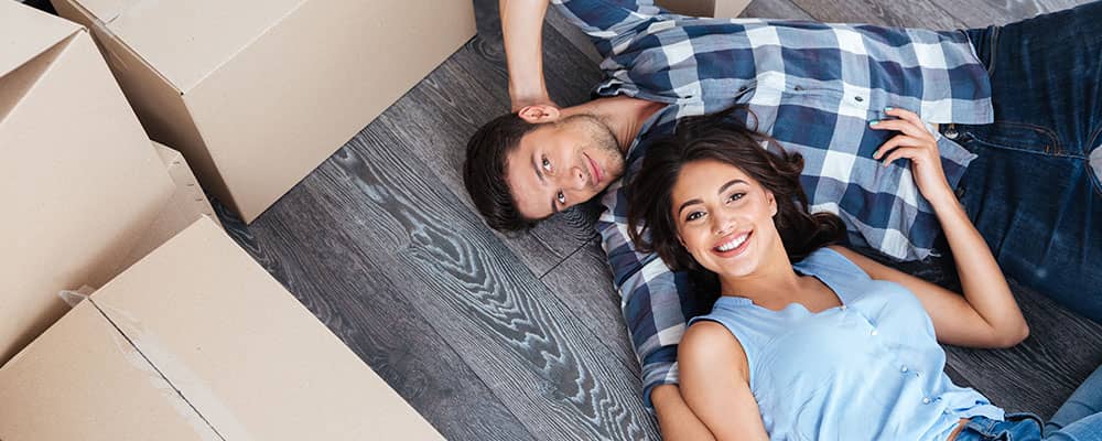 couple lying on hardwood floor surrounded by moving boxes